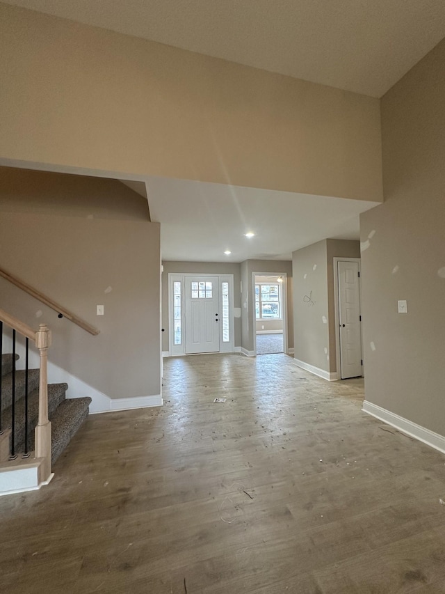 unfurnished living room with stairs, wood finished floors, and baseboards