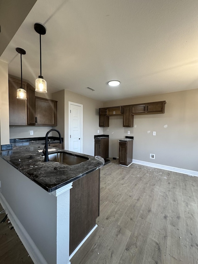 kitchen featuring dark brown cabinets, baseboards, light wood-type flooring, a peninsula, and a sink