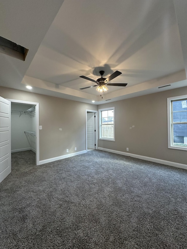 unfurnished bedroom featuring carpet, baseboards, ceiling fan, a spacious closet, and a raised ceiling