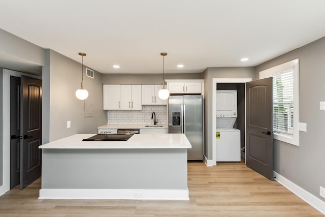 kitchen featuring pendant lighting, stainless steel fridge with ice dispenser, light wood-type flooring, stacked washing maching and dryer, and white cabinetry