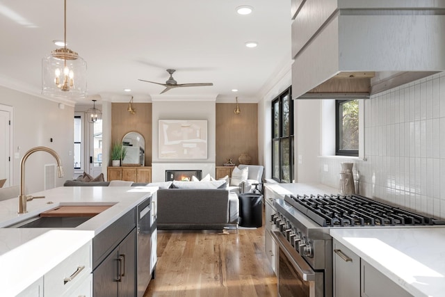 kitchen with sink, custom exhaust hood, crown molding, high end stainless steel range oven, and pendant lighting