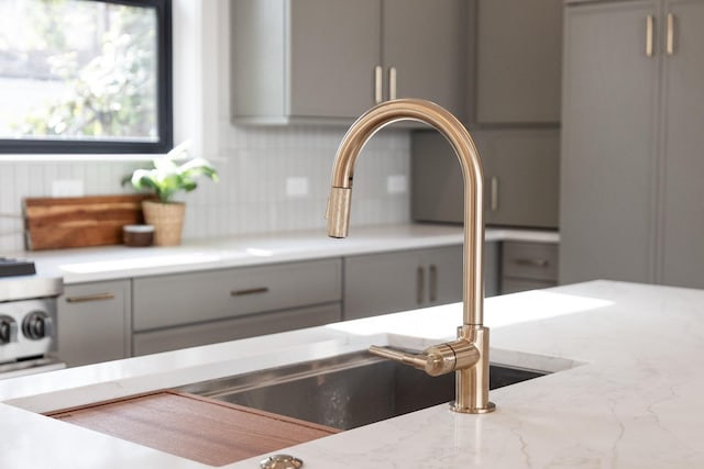 interior details with light stone counters, sink, tasteful backsplash, and gray cabinetry