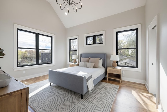 bedroom with an inviting chandelier, light hardwood / wood-style flooring, and high vaulted ceiling