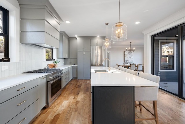 kitchen with gray cabinetry, decorative light fixtures, light wood-type flooring, an island with sink, and stainless steel appliances