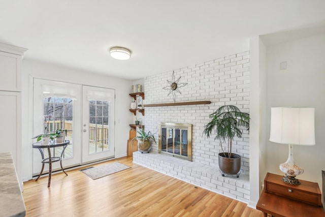 living room featuring light hardwood / wood-style flooring, french doors, and a brick fireplace