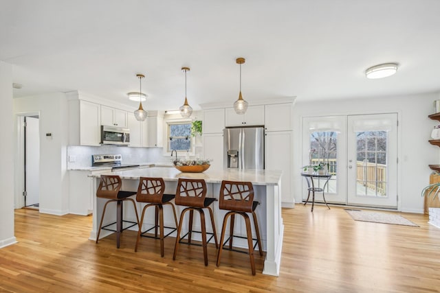 kitchen featuring light wood-type flooring, stainless steel appliances, decorative light fixtures, white cabinets, and a center island