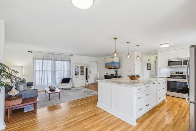 kitchen featuring light wood-type flooring, stainless steel appliances, pendant lighting, white cabinets, and a kitchen island