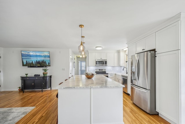 kitchen featuring stainless steel appliances, white cabinets, light hardwood / wood-style floors, a kitchen island, and hanging light fixtures