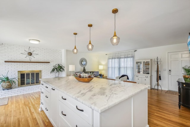 kitchen featuring a center island, a brick fireplace, light hardwood / wood-style flooring, pendant lighting, and white cabinets