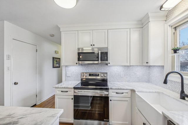 kitchen with light stone counters, stainless steel appliances, white cabinetry, and sink