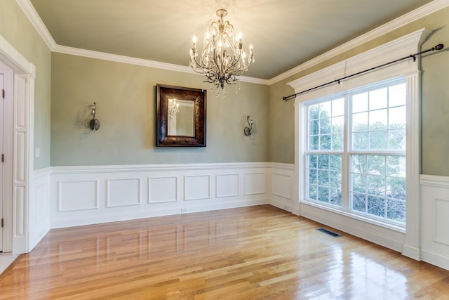 empty room featuring crown molding, light wood-type flooring, and an inviting chandelier