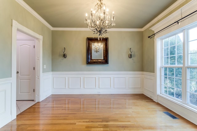 unfurnished room with a wealth of natural light, ornamental molding, light wood-type flooring, and an inviting chandelier