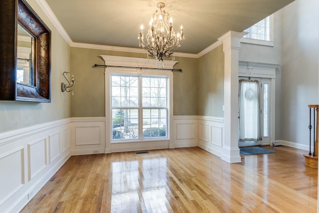 unfurnished dining area featuring light wood-type flooring, ornate columns, crown molding, and a notable chandelier