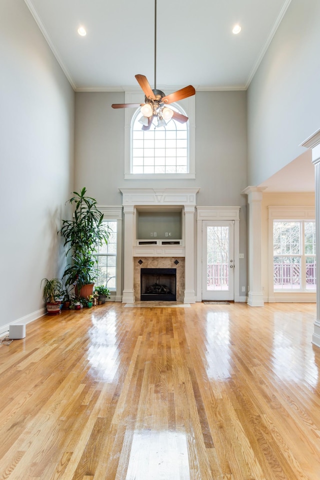 unfurnished living room featuring decorative columns, ceiling fan, ornamental molding, and a tiled fireplace