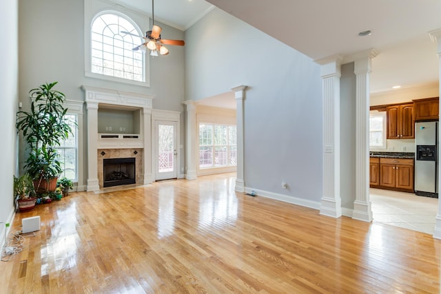 unfurnished living room featuring a tile fireplace, light hardwood / wood-style flooring, ceiling fan, ornate columns, and ornamental molding