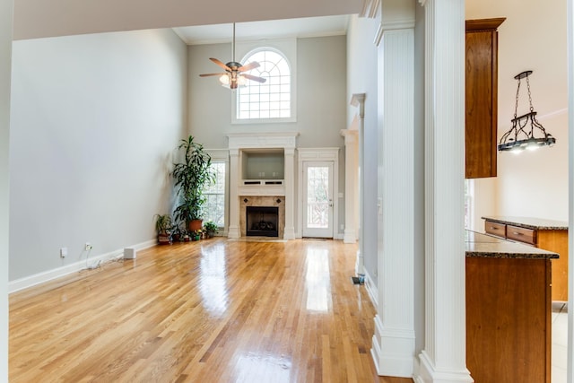 unfurnished living room with ceiling fan, crown molding, a high ceiling, and light hardwood / wood-style flooring