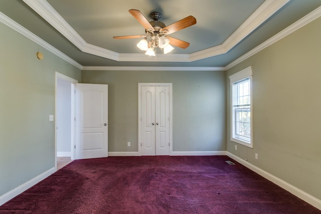 unfurnished bedroom featuring a tray ceiling, ceiling fan, dark carpet, and ornamental molding