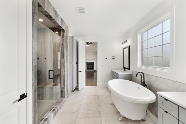 bathroom featuring separate shower and tub, ceiling fan, vanity, and tile walls