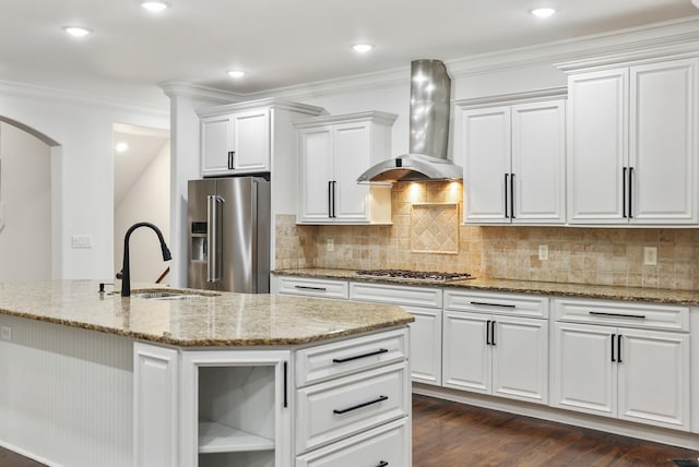 kitchen with wall chimney exhaust hood, stainless steel appliances, a kitchen island with sink, sink, and white cabinetry