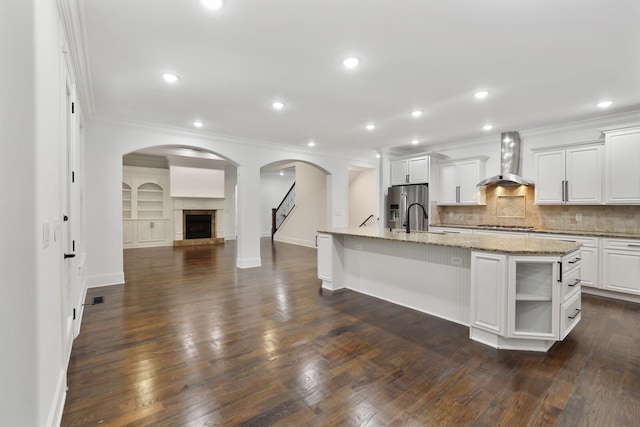 kitchen with stainless steel fridge with ice dispenser, a center island with sink, dark hardwood / wood-style floors, and wall chimney exhaust hood