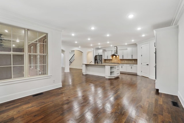 kitchen with wall chimney exhaust hood, dark hardwood / wood-style floors, stainless steel fridge, a center island with sink, and white cabinets