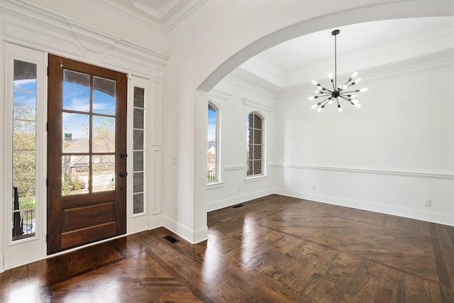 foyer with dark parquet floors, ornamental molding, and a chandelier