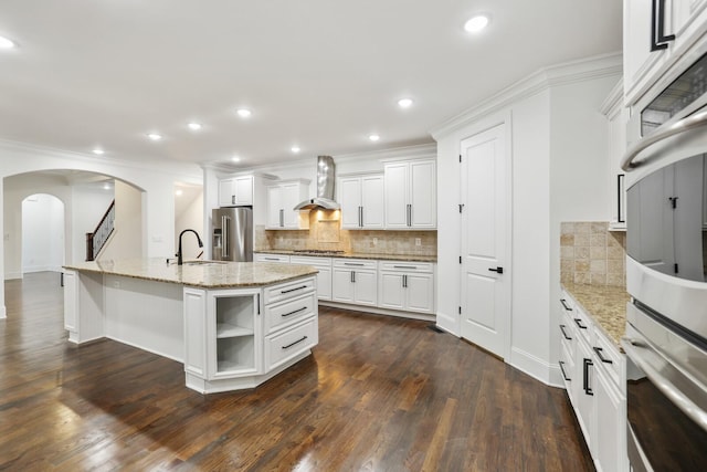 kitchen featuring a center island with sink, dark hardwood / wood-style floors, wall chimney exhaust hood, appliances with stainless steel finishes, and white cabinetry