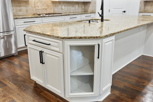 kitchen featuring light stone counters, dark wood-type flooring, stainless steel appliances, and an island with sink