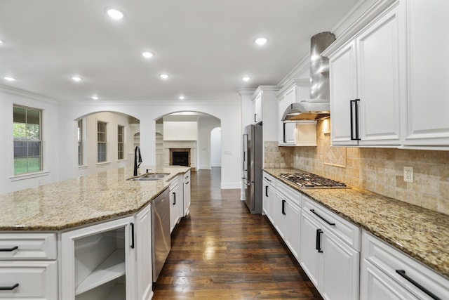 kitchen with sink, dark wood-type flooring, wall chimney range hood, white cabinets, and appliances with stainless steel finishes