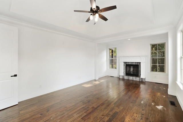 unfurnished living room featuring a raised ceiling, crown molding, ceiling fan, a premium fireplace, and dark hardwood / wood-style flooring