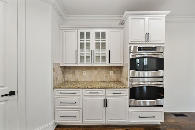 kitchen with white cabinets, decorative backsplash, light stone countertops, double oven, and dark hardwood / wood-style flooring