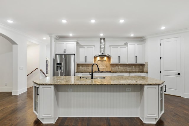 kitchen with stainless steel refrigerator with ice dispenser, a large island with sink, dark wood-type flooring, and wall chimney range hood