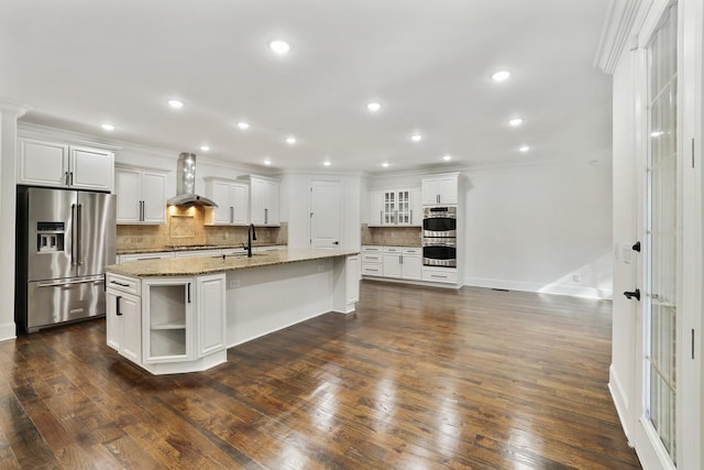 kitchen featuring wall chimney exhaust hood, stainless steel appliances, dark hardwood / wood-style floors, a center island with sink, and white cabinets