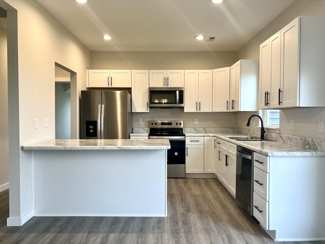 kitchen featuring hardwood / wood-style floors, sink, white cabinetry, kitchen peninsula, and stainless steel appliances