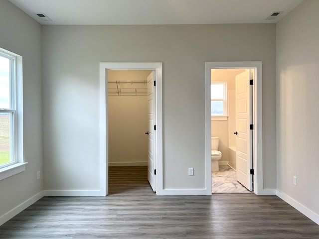 unfurnished bedroom featuring a closet, ensuite bath, a walk in closet, and hardwood / wood-style floors