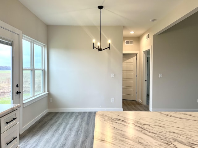 unfurnished dining area with wood-type flooring and a notable chandelier