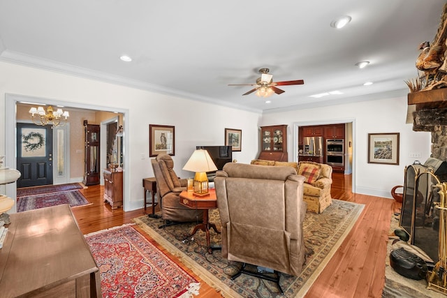 living room featuring hardwood / wood-style flooring, ceiling fan with notable chandelier, and ornamental molding