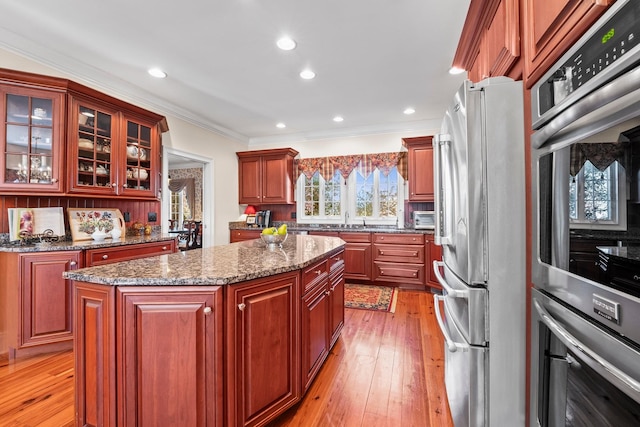 kitchen featuring appliances with stainless steel finishes, ornamental molding, sink, light hardwood / wood-style flooring, and a center island