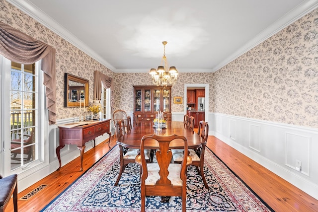 dining space with hardwood / wood-style flooring, crown molding, and an inviting chandelier