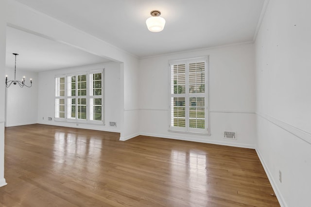 empty room featuring crown molding, hardwood / wood-style floors, and a chandelier