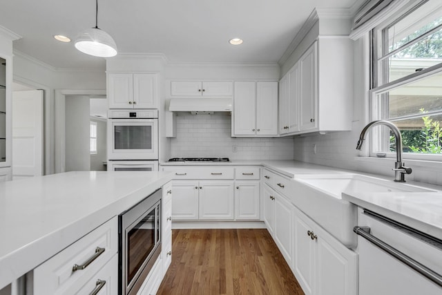 kitchen with hardwood / wood-style floors, stainless steel microwave, premium range hood, white cabinets, and decorative light fixtures