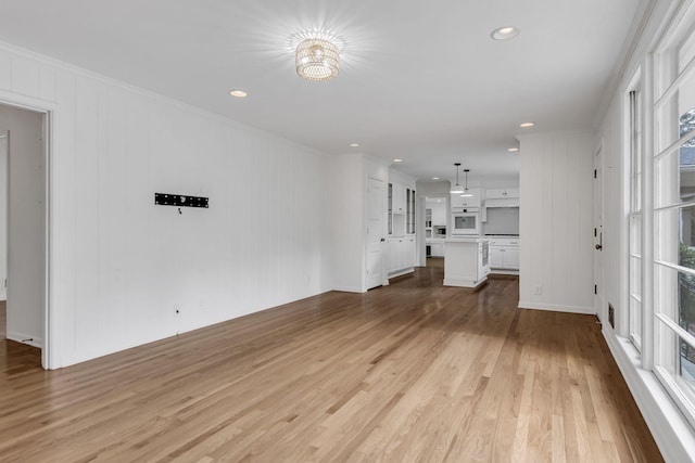 unfurnished living room featuring light hardwood / wood-style floors, crown molding, and a chandelier