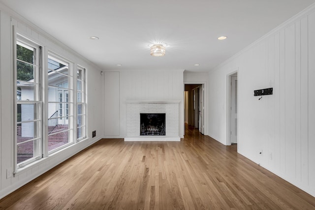 unfurnished living room featuring a brick fireplace, crown molding, and light hardwood / wood-style flooring