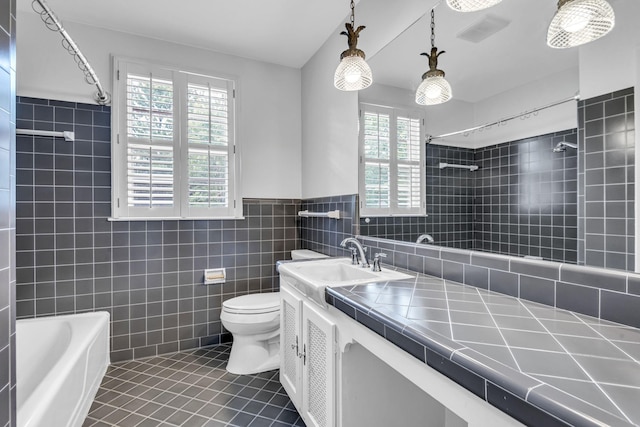 full bathroom with vanity, tile walls, tile patterned flooring, toilet, and tiled shower / bath