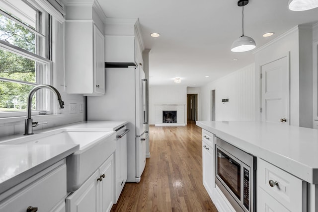 kitchen with white cabinetry, stainless steel microwave, hanging light fixtures, a brick fireplace, and dark hardwood / wood-style floors