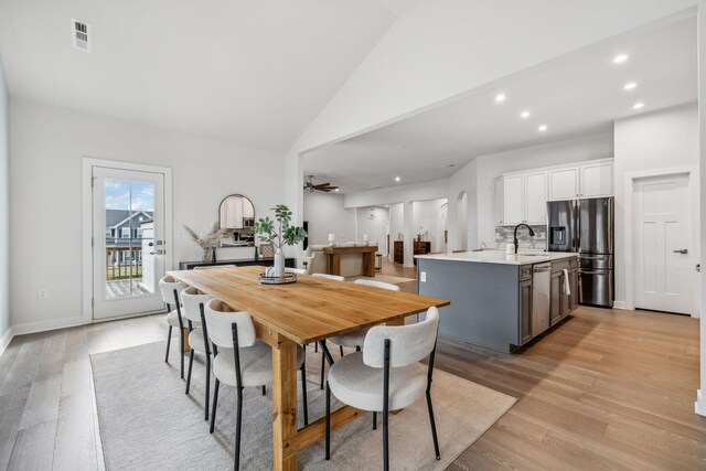 dining area featuring ceiling fan, sink, high vaulted ceiling, and light hardwood / wood-style floors