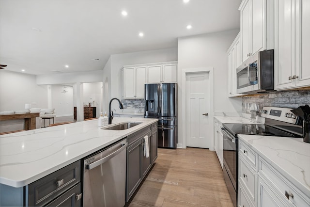 kitchen with light stone countertops, light wood-type flooring, stainless steel appliances, and sink