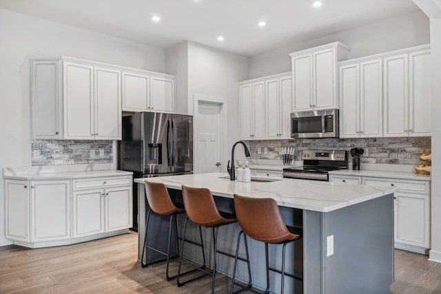 kitchen featuring appliances with stainless steel finishes, light wood-type flooring, sink, a center island with sink, and white cabinets