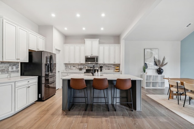 kitchen with tasteful backsplash, white cabinets, stainless steel appliances, and light wood-type flooring