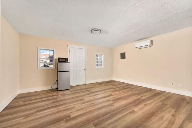 spare room with an AC wall unit, a textured ceiling, and light hardwood / wood-style flooring